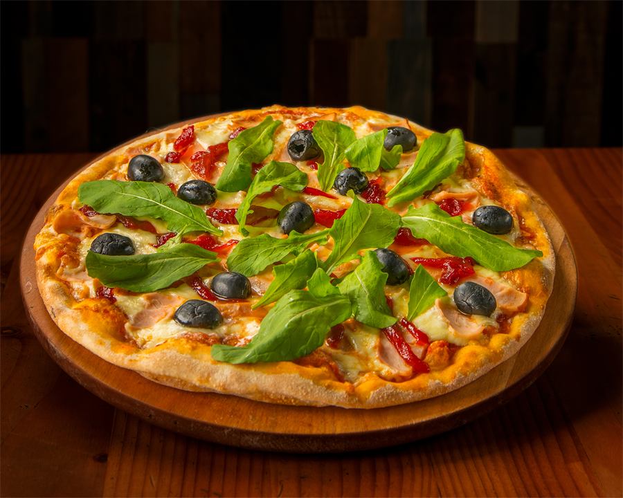 Pizza Luciana — Base pomodoro, mozzarella, jamón de pierna, pimentón caramelizado, aceitunas negras y rúcula.